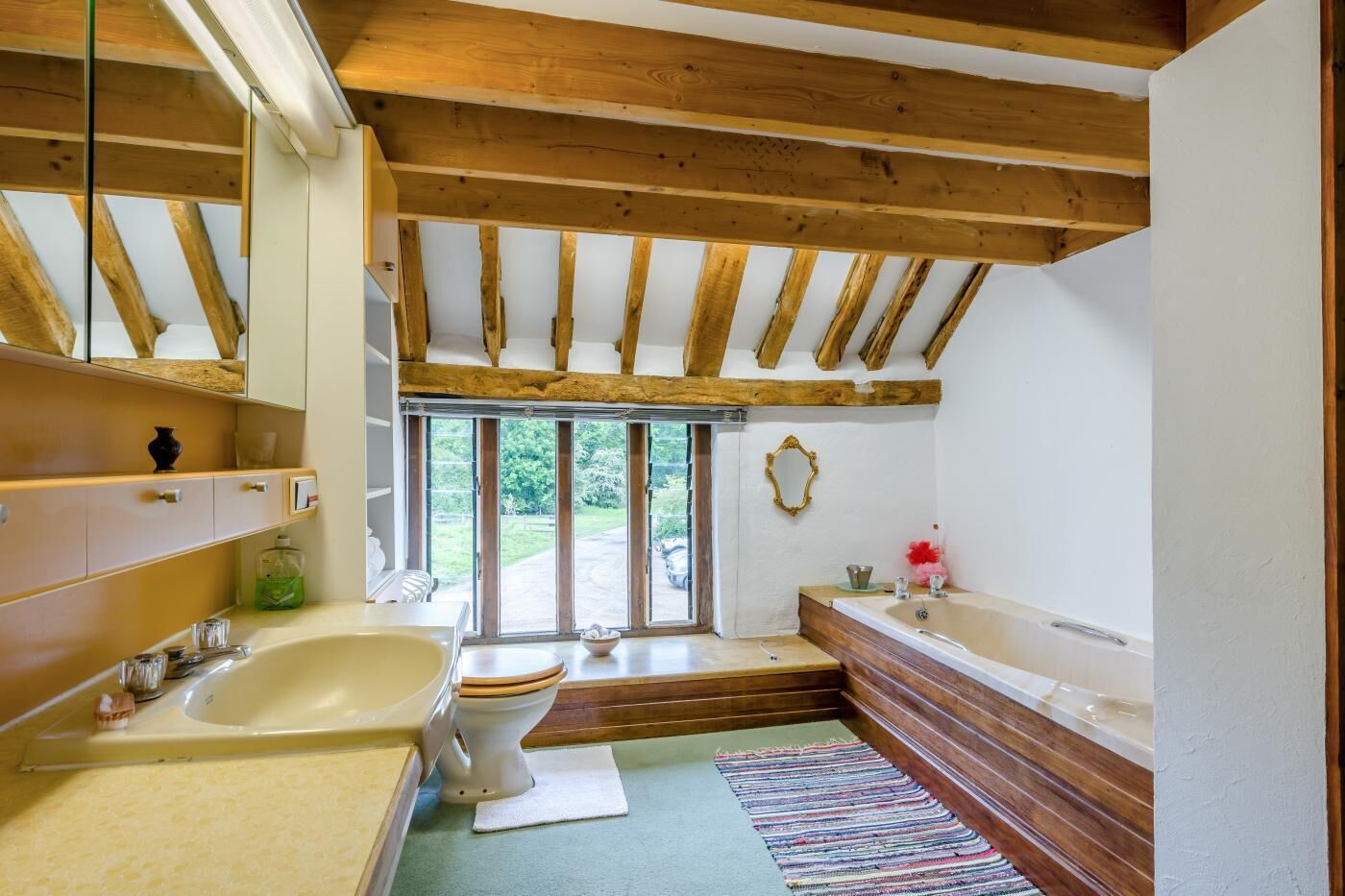 Een badkamer met een houten plafond, een bad, een toilet en een raam.