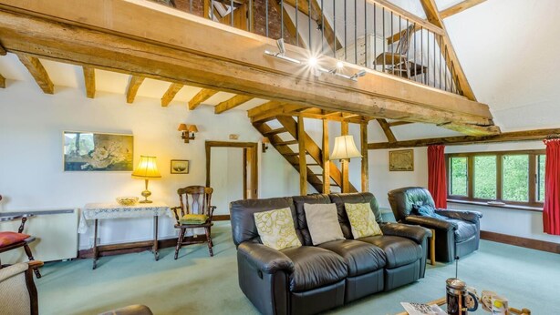 Un vaste espace de vie doté d’un haut plafond, de poutres en bois, d’un escalier et d’une grande fenêtre.