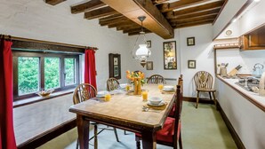 Un espace repas comprenant une table en bois, des chaises et un coin cuisine équipé d’un évier et d’ustensiles.