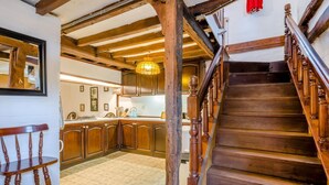 Un escalier en bois mène à une cuisine dotée de meubles de rangement en bois et d’un sol carrelé.