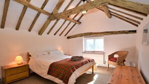 Ein Schlafzimmer mit einem Bett, einem Nachttisch, einem Sessel, einem Holztisch und einem Fenster.