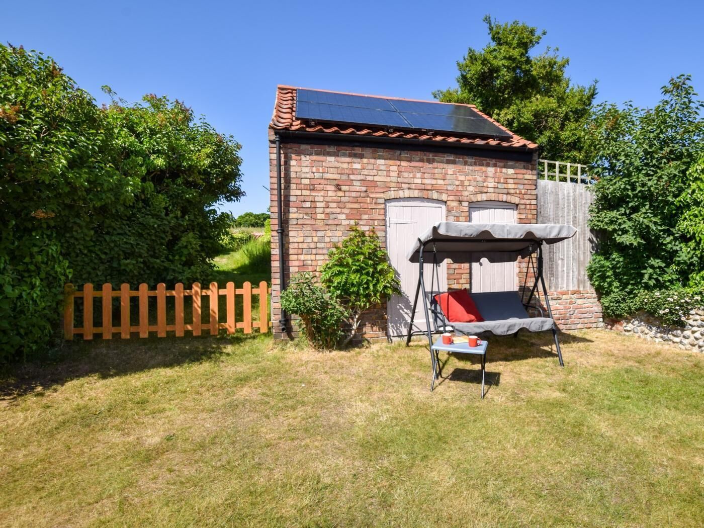 A brick building with a solar panel, a swing chair, and a wooden fence.