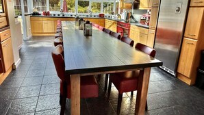 A modern kitchen with a long dining table, wooden cabinets, and a large window. - 10 Bed in Lampeter (oc-pontv) (Lampeter)
