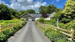 A rural road leading to a stone farmhouse with a white exterior, surrounded by lush greenery and a wooden fence. - 10 Bed in Lampeter (oc-pontv) (Lampeter)