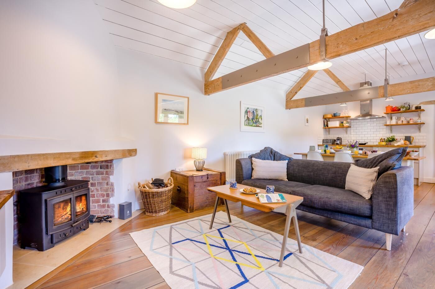 Een gezellige woonkamer met een open haard, een bank, een salontafel en een keuken in de achtergrond.