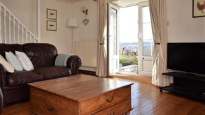 Ein Wohnzimmer mit einem braunen Ledersofa, einem Holztisch, einem Fernsehschrank und Blick durch eine Glastür.