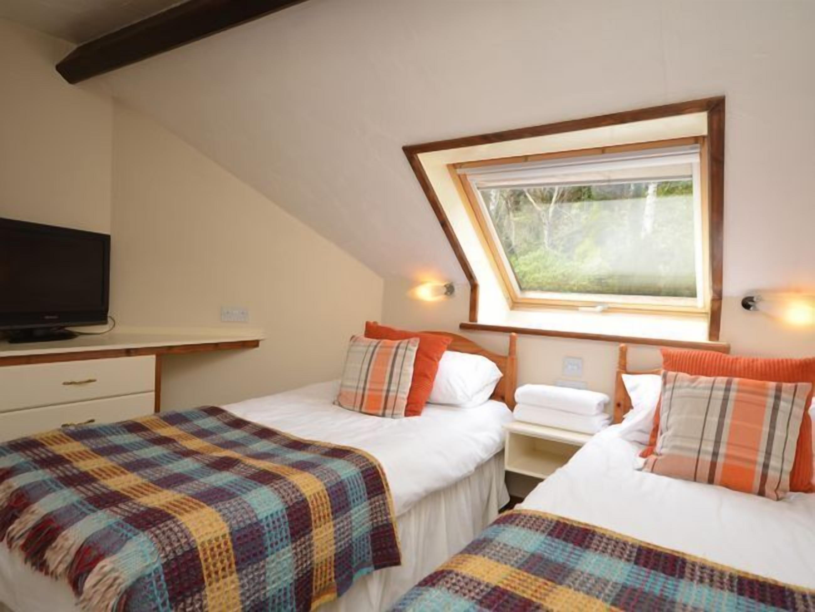 Ein Schlafzimmer mit zwei Betten, einem Fernseher und einem Fenster.
