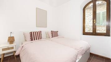 Un dormitorio con dos camas, una mesita de noche con lámpara, una ventana con persianas y un cuadro colgado en la pared.