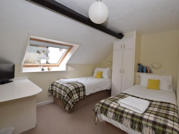 A bedroom with two beds, a desk, a wardrobe, and a skylight.
