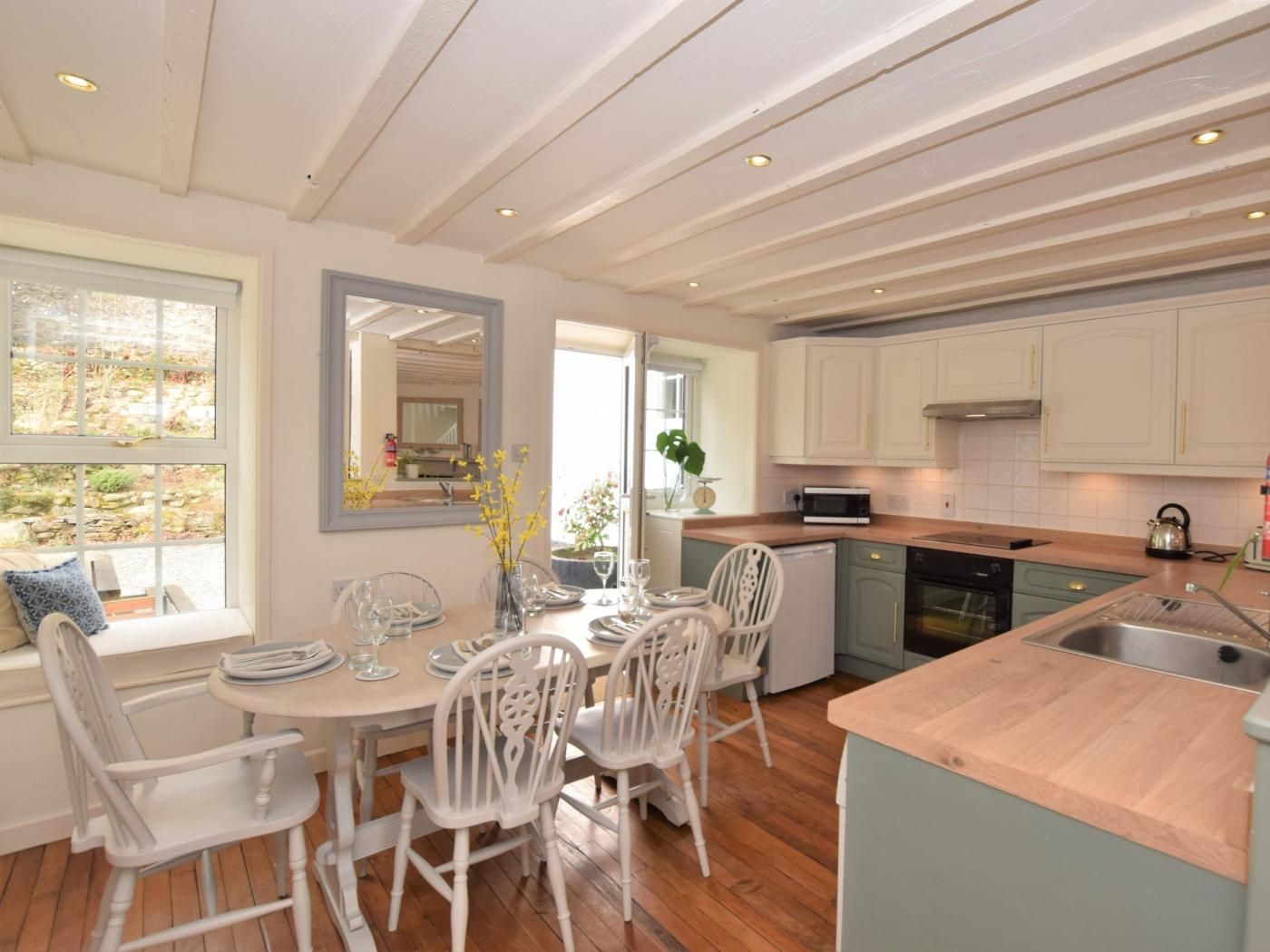 A modern kitchen with white cabinetry, a wooden countertop, and a dining area with white chairs and a table.