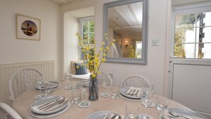 Ein Esszimmer mit einem für sechs Personen gedeckten Tisch, einer Vase mit gelben Blumen und einem Spiegel an der Wand.