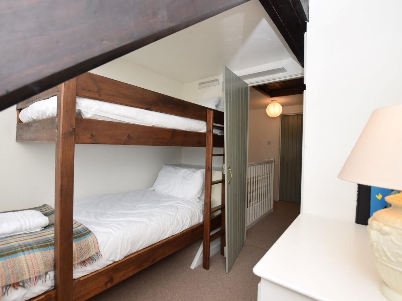 Ein Schlafraum mit Etagenbett, Holzrahmen, weißer Matratze und gestreifter Decke.