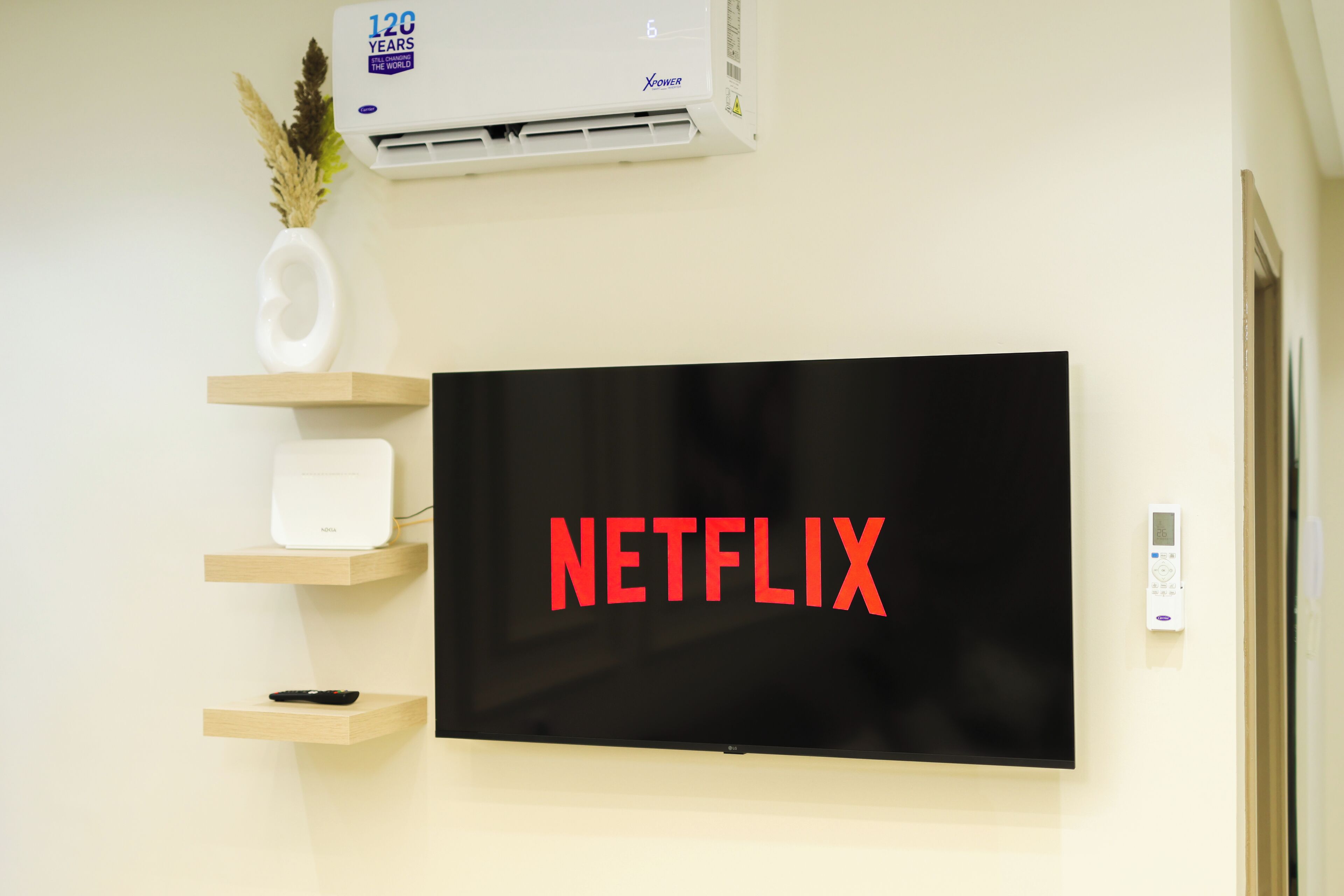 Een aan de muur bevestigde televisie met het Netflix-logo, een witte airconditioner en een thermostaat.