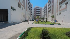 A residential building with balconies, a gated entrance, and a landscaped area with palm trees. - TGV 7 min Corniche Plage WiFi fibre (Tanger)