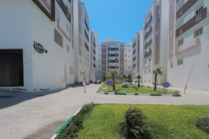 Un edificio residencial con balcones, entrada porticada y una zona ajardinada con palmeras.