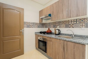 A kitchen with wooden cabinets, a stove, an oven, a sink, and a patterned backsplash. - TGV 7 min Corniche Plage WiFi fibre (Tanger)