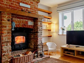 A cozy room with a brick fireplace, a television, and a bookshelf. - 2 Bed in Northrepps (oc-dain8) (Northrepps)