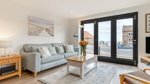 Een moderne woonkamer met een grijze bank, een houten salontafel en uitzicht door een grote glazen deur.