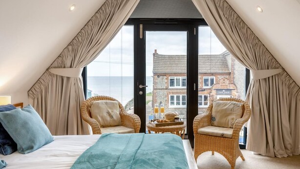 Een slaapkamer met een bed, twee rieten stoelen, een kleine tafel en uitzicht op een gebouw door een glazen deur.