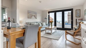 Een moderne woonkamer met een eethoek, een bank, een salontafel en uitzicht op zee door grote ramen.