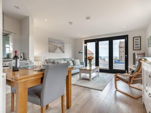 Ein modernes Wohnzimmer mit Essbereich, einer Couch, einem Couchtisch und Meerblick durch große Fenster.