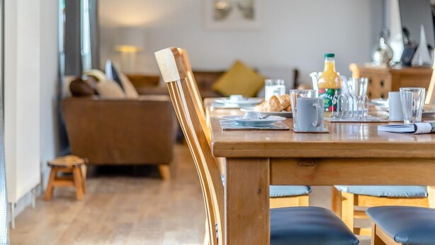 Ein Essbereich mit Holztisch, Stühlen, einer Couch und einer Frühstücksvorrichtung, darunter Croissants und Saft.