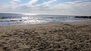 Ein Strand mit sichtbaren Fußspuren, einem klaren Himmel und ruhiger See.