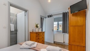 Ein Schlafzimmer mit einem Bett, einem Holzschrank, einem Fernseher, einer Kommode und einem Fenster mit Vorhängen.