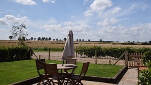 Eine Terrasse im Freien mit Tisch und Stühlen, einem Sonnenschirm und Blick auf eine ländliche Landschaft mit Feldern und Bäumen.