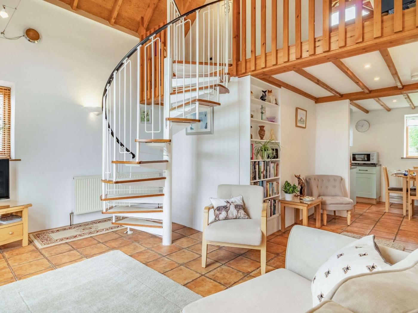 Una sala de estar con una escalera en espiral, un sofá, un sillón, una estantería y un comedor.