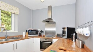 Ett modernt kök med vita skåp, en rostfri köksfläkt, en mikrovågsugn, en ugn och en kaffemaskin.