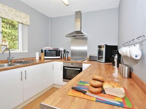 Eine moderne Küche mit weißen Schränken, einer Edelstahl-Dunstabzugshaube, einer Mikrowelle, einem Backofen und einer Kaffeemaschine.