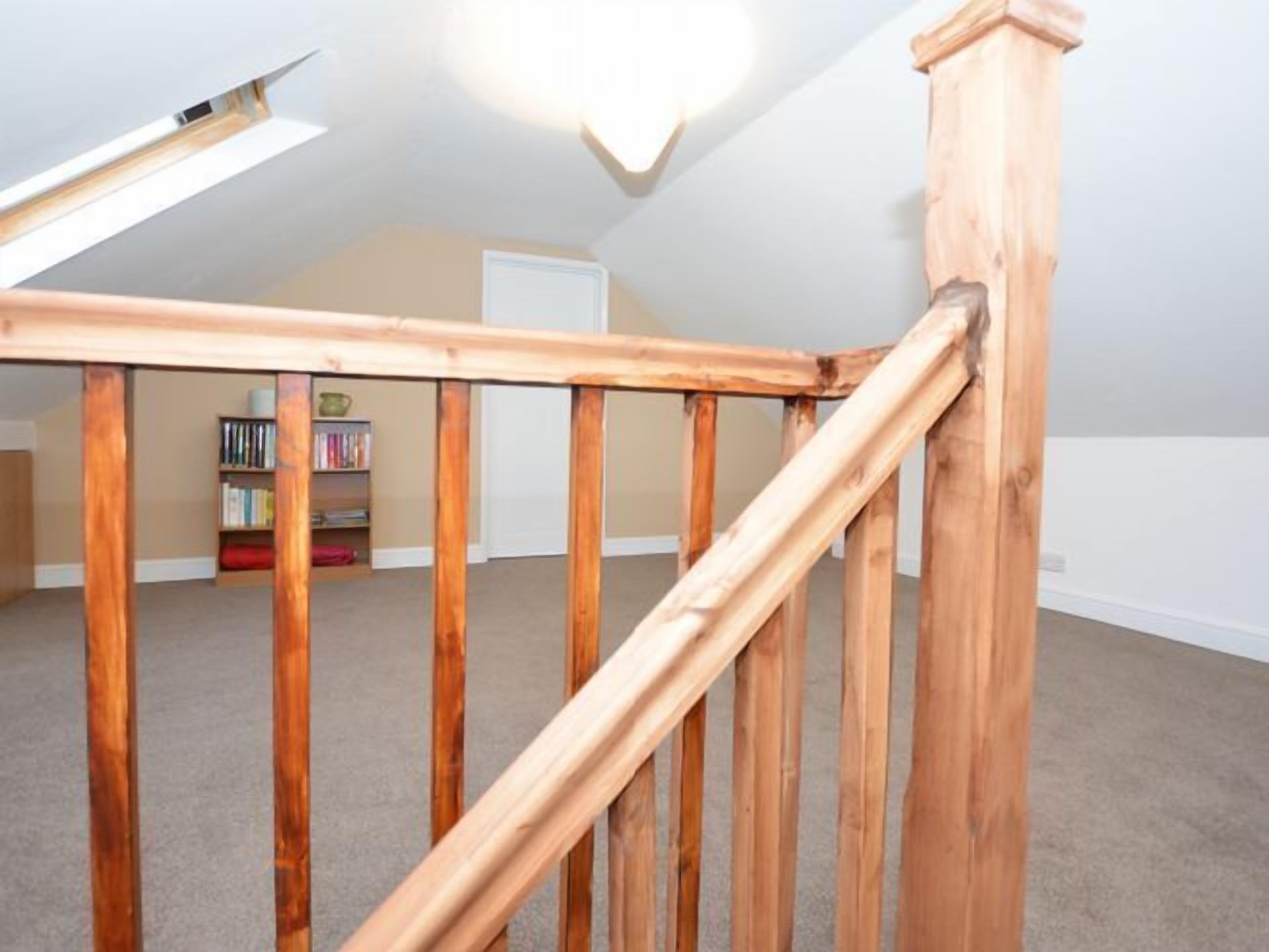 Un escalier en bois dans une pièce dont le sol est recouvert d’une moquette, avec une bibliothèque et une porte visible au fond.