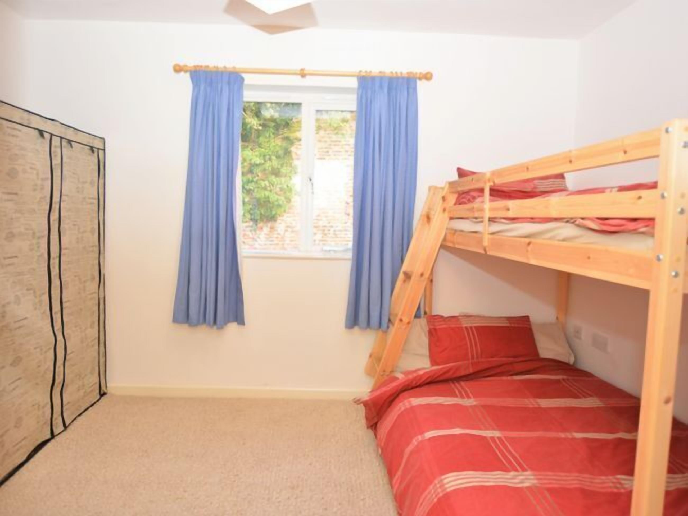 Een slaapkamer met een stapelbed, raam, gordijnen en een kledingkast.