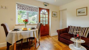 A dining area with a table set for two, a red door, and a sofa with a drink holder. - 1 Bed in Ilfracombe (oc-fiddl) (Berrynarbor)