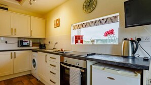 A compact kitchen with white cabinets, a microwave, a kettle, and a window with a view. - 1 Bed in Ilfracombe (oc-fiddl) (Berrynarbor)