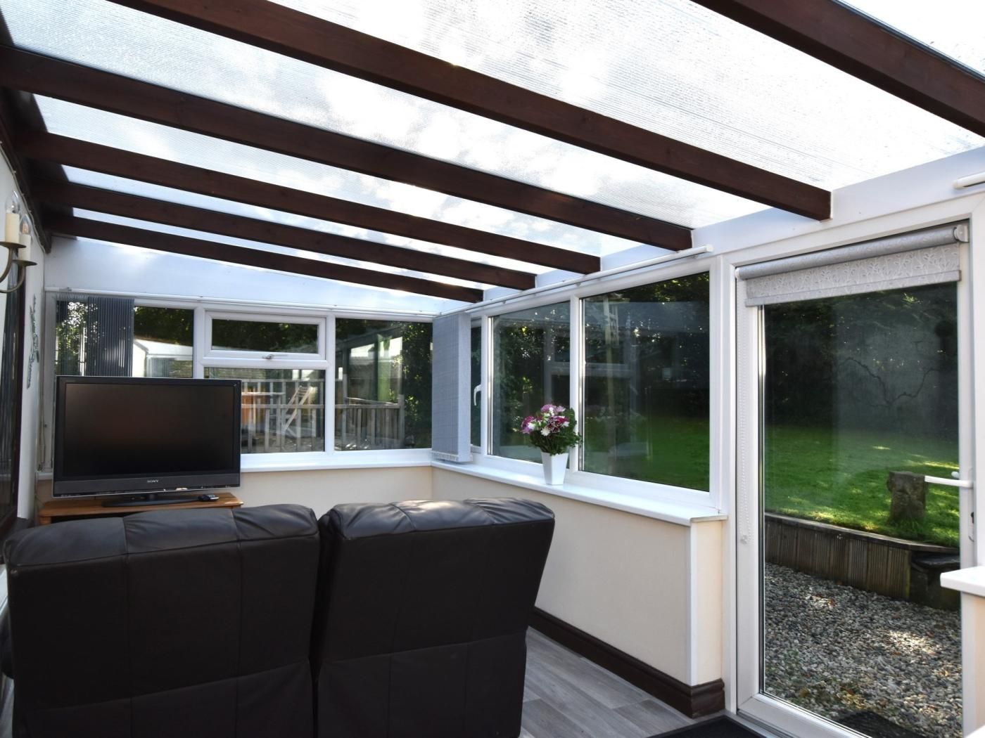 Eine überdachte Terrasse mit Fernseher, Sitzgelegenheiten und großen Fenstern.