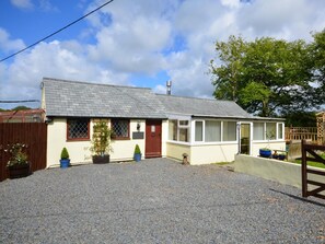 A single-story house with a gravel driveway, a wooden fence, and a large tree in the background. - 1 Bed in Holsworthy (oc-wscot) (Pancrasweek)