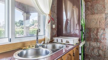 A kitchen with a double sink, wooden cabinets, a marble backsplash, and a view through the window.