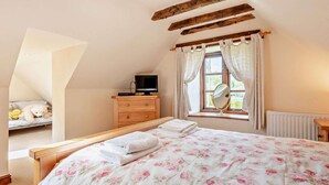 Une chambre à coucher avec un lit, une commode, un téléviseur, une fenêtre avec des rideaux et un radiateur.
