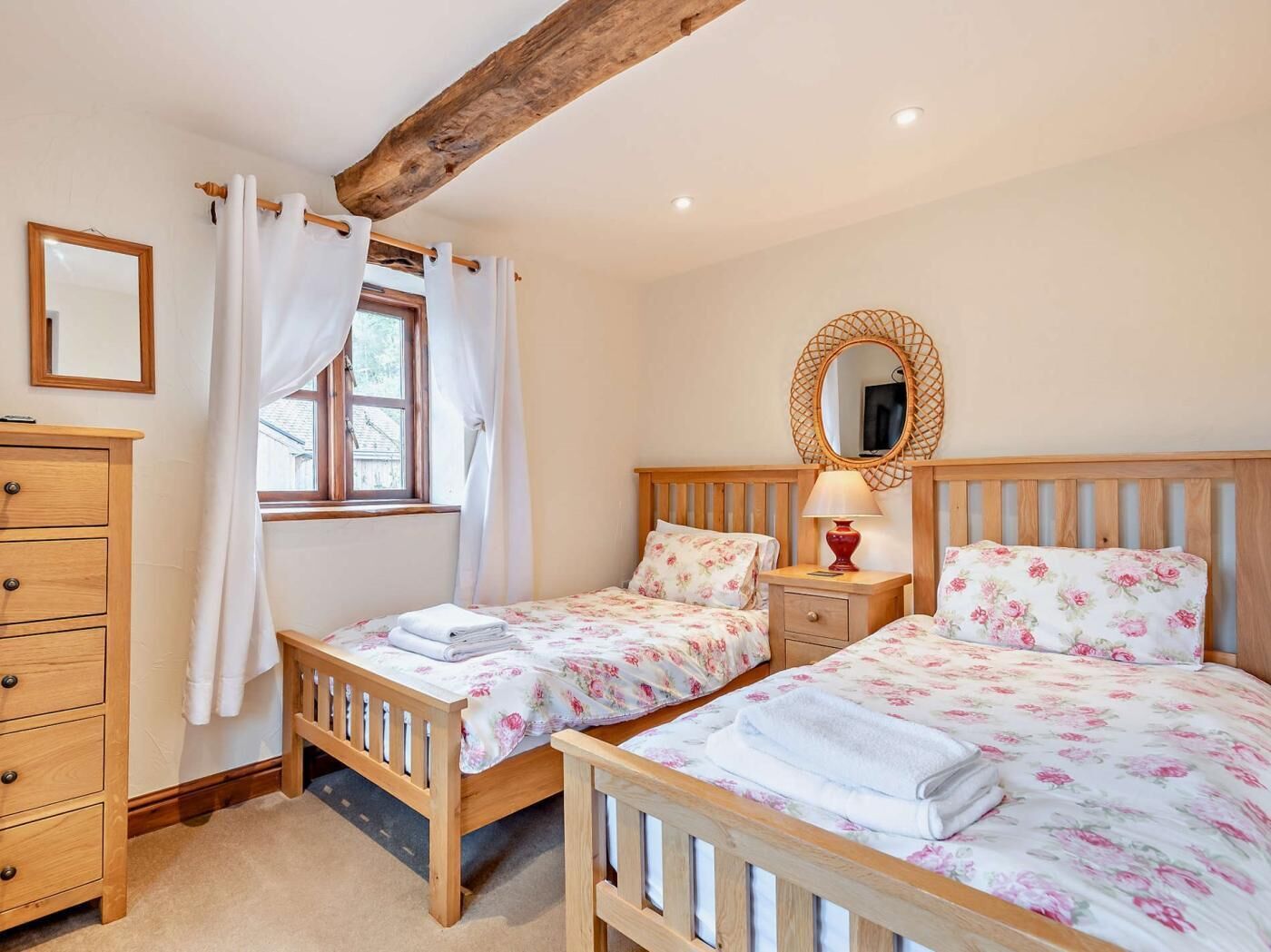 Een slaapkamer met twee bedden, een houten dressoir, een spiegel en een raam met gordijnen.