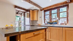 Une cuisine avec des meubles de rangement en bois, un plan de travail et une fenêtre ornée d’une maquette de bateau.