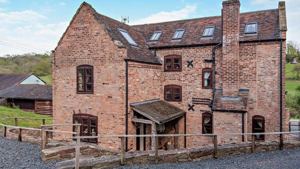 Un bâtiment historique en briques, doté de nombreuses fenêtres, d’une cheminée et d’un petit porche.