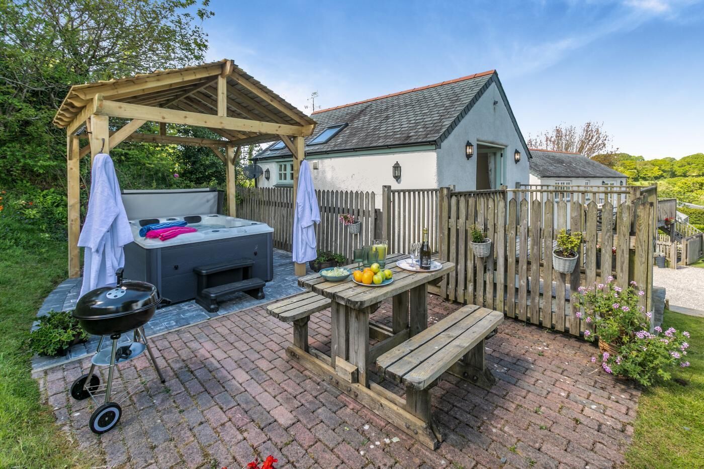 Un patio trasero con un jacuzzi, una parrilla, una mesa de madera y un banco de picnic.