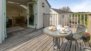 Een terras buiten, met een tafel gedekt voor thee, en een eetgedeelte zichtbaar door een open deur, met een houten hek.