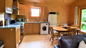 A compact kitchen with wooden cabinets, a washing machine, and a dining area with a table and chairs.