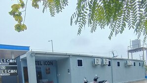 A building with a sign reading 'TEL ICON HOTEL,' a scooter parked in front, and a tree with green leaves overhead.