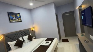 A modern hotel room with a bed, bedside tables, a flat-screen TV, a painting on the wall, and a door.