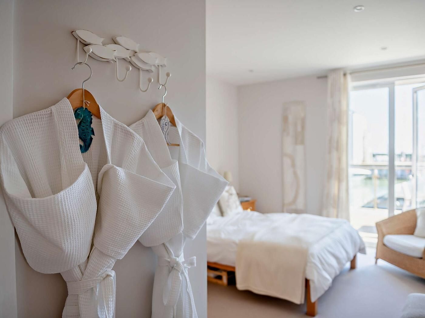 A hotel room with a bed, a seating area with a chair, and a wall-mounted robe rack with towels.