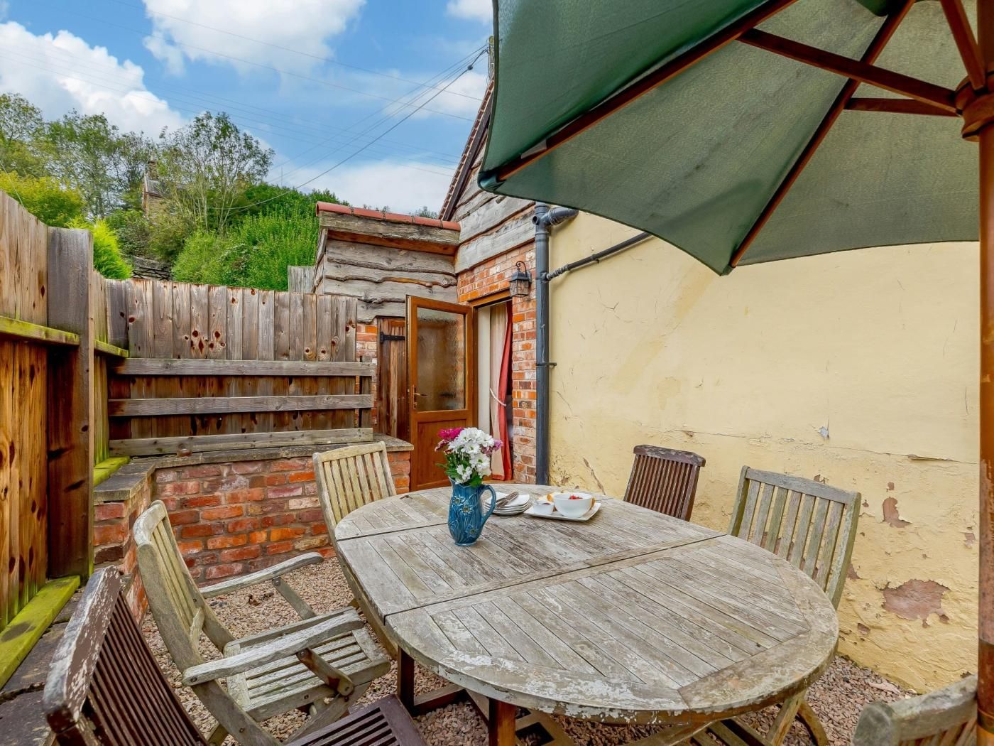 A wooden patio with a round table, chairs, and a green umbrella.